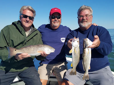 Three anglers holding their catch sitting on the bow of the boat.